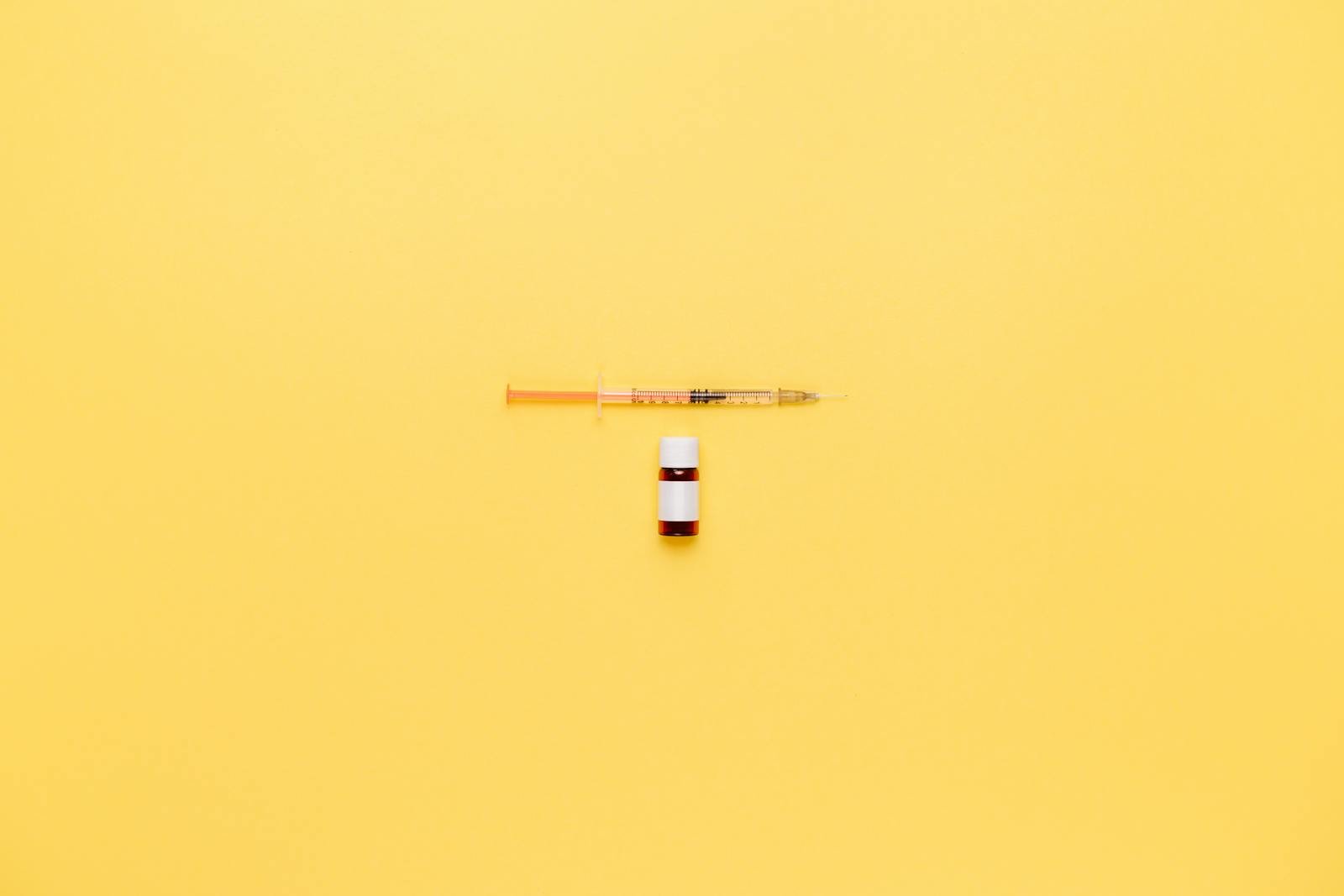 Minimalist image of a syringe and vaccine vial on a vibrant yellow background.