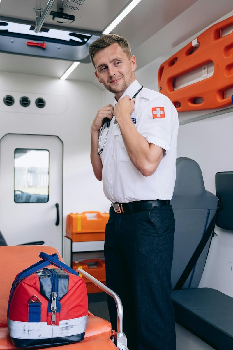 Confident paramedic in uniform stands inside an ambulance, holding a stethoscope.