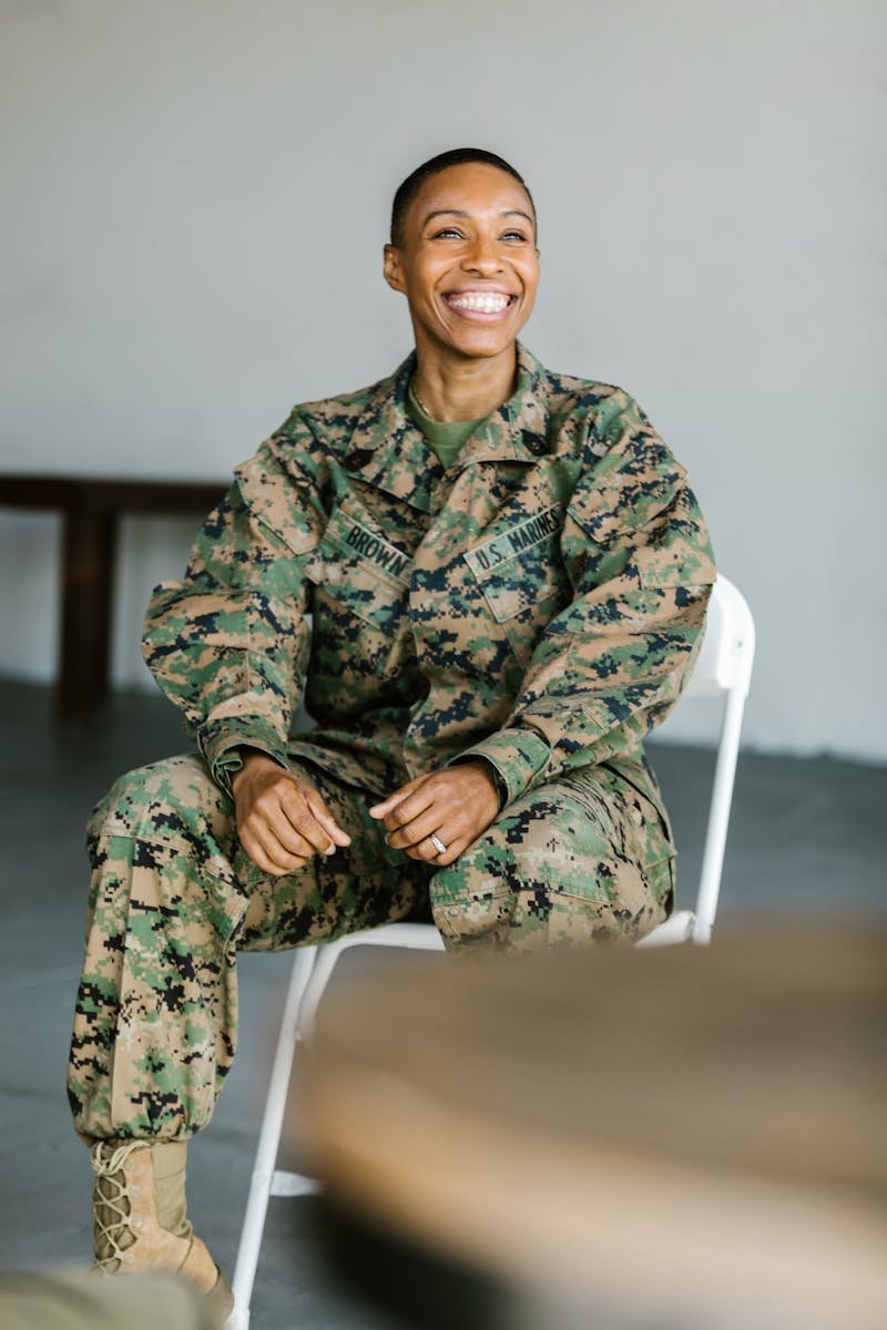 Cheerful female soldier in uniform sitting and smiling indoors.