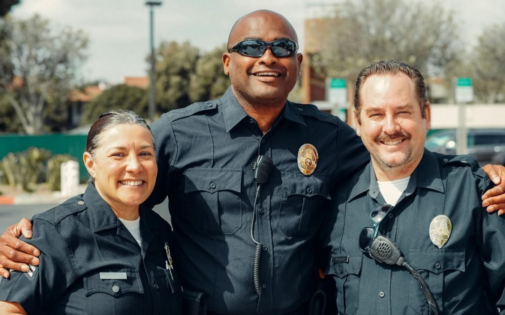 Three police officers smiling and posing in an outdoor setting, showcasing camaraderie in law enforcement.